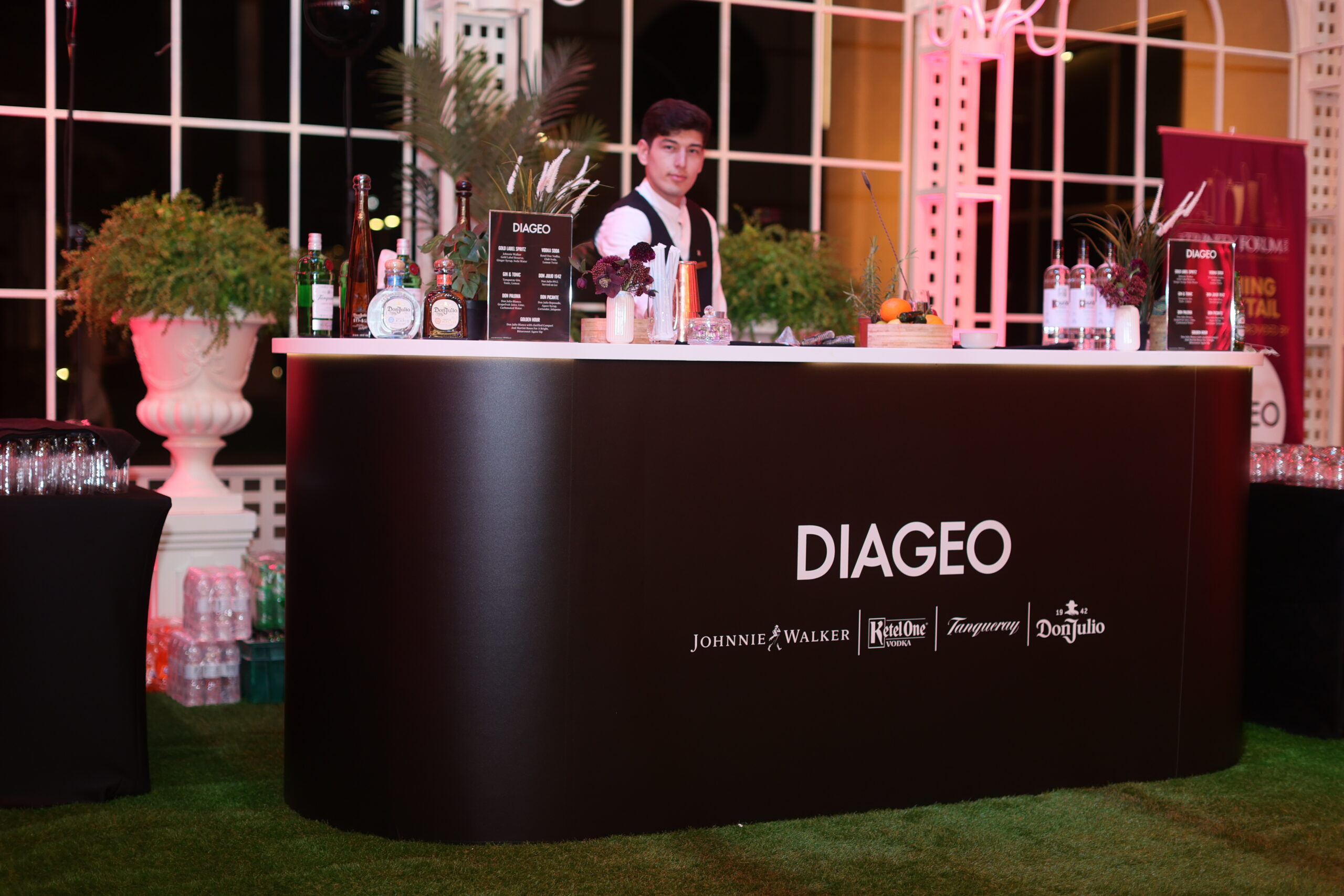 Bar counter with assorted liquor bottles and a bartender standing behind, DIAGEO branding on the front panel.